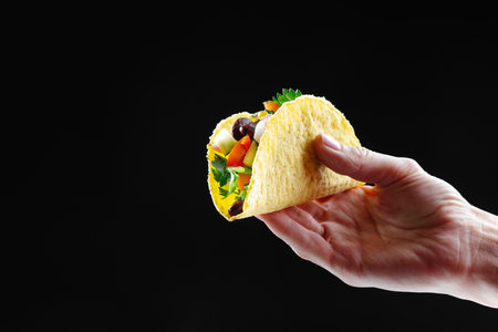 A womans hand holds a taco with vegetables and a black background isolate. Blank space for textの写真素材