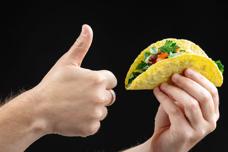 A hand holds a taco with vegetables and a black background isolate. Empty space for text. Clean...