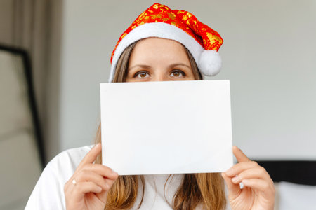 A girl is holding a blank letter to Santa Claus. Woman in a Christmas hat holding a letter in front of her. Mockupの写真素材