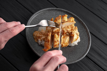 Hands with a knife and fork. Man eats chicken breast in cream sauce and rice.の写真素材