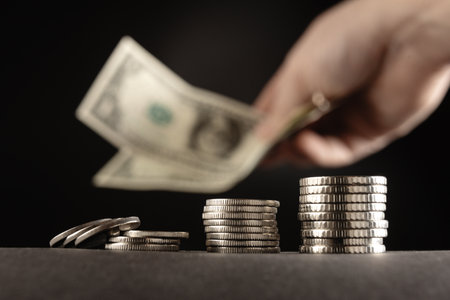 Social Assistance in the United States. Coins and hand with dollars on dark background. The concept of aid moneyの写真素材