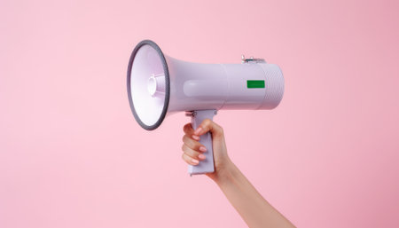 Female hand holding a megaphone on a pink background with copy space.の素材