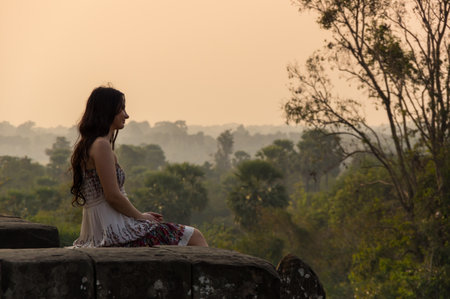 ANGKOR WAT, CAMBODIA - JANUARY 28, 2015: Young beautiful woman watching sunset at the top of Phnom Bakheng at Angkor, Cambodiaのeditorial素材