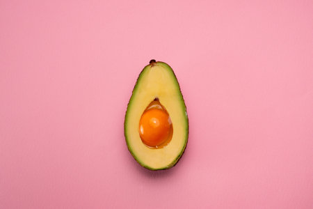 Avocado with egg yolk in middle on pink background. Creative food concept