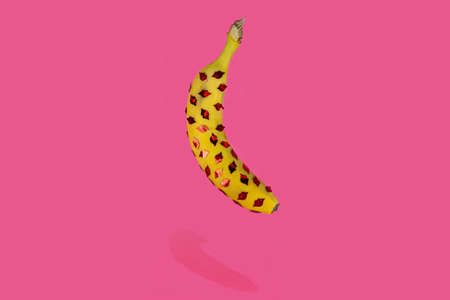 Floating banana with little kiss lips on it. Pink background. Creative love conceptの写真素材