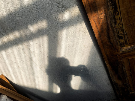 Drop shadow of a man getting a selfie, projected by the light of a sunset on a cement and wood, in...