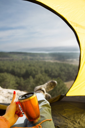 View from the tent. Cool trip. A girl sitting in a tent holds a thermocup in her hand, shows like....