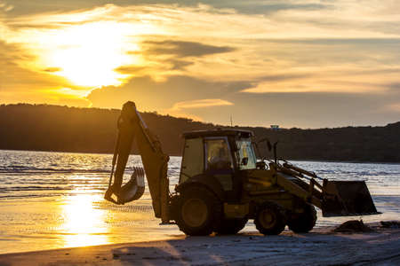 Silhouetted Wheel loader Excavator unloading sand during earthmoving works on the beachの写真素材