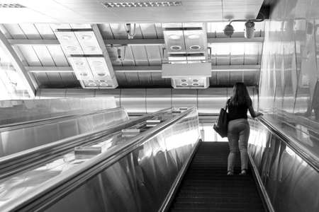 woman going up escalator at metro station, black and white photoの写真素材
