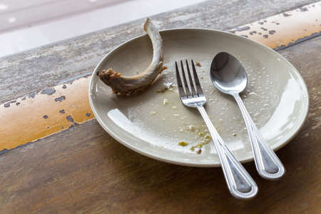 finished meal after party, rib bone in empty plate with spoon and fork on wood tableの写真素材