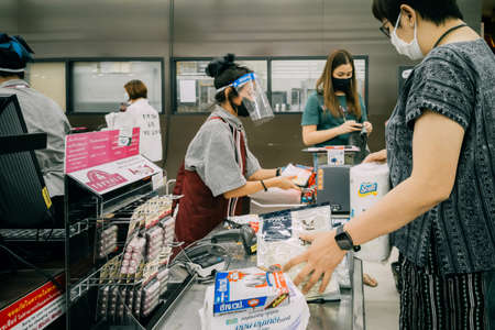 Bangkok, Thailand - June 30, 2020 :  asian woman shoppers and cashier are wearing hygiene face mask to protect from coronavirus pandemic or covid-19 virus outbreak in supermarket . social distancing.のeditorial素材