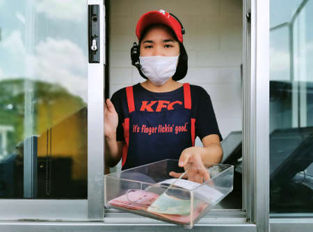 Bangkok, Thailand - June 30, 2020 : KFC fast food cashier in drive thru service waring hygiene face mask to protect coronavirus pandemic or covid-19 virus outbreak is giving money change to customer.のeditorial素材