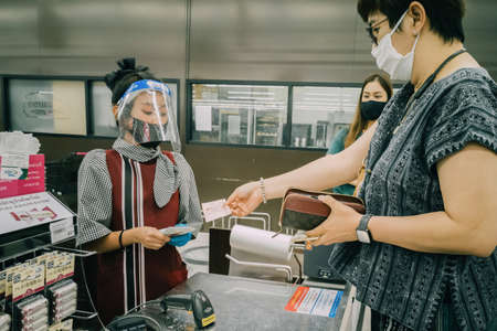 Bangkok, Thailand - October 1, 2020 :  asian woman shoppers and cashier wearing hygiene face mask to protect from coronavirus pandemic or covid-19 virus outbreak in supermarket . social distancing.のeditorial素材