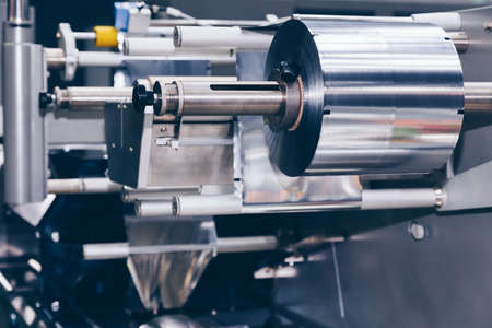 roll of aluminum foil for food packaging on the automatic packing machine in food product factory. industrial and technology concept.の写真素材