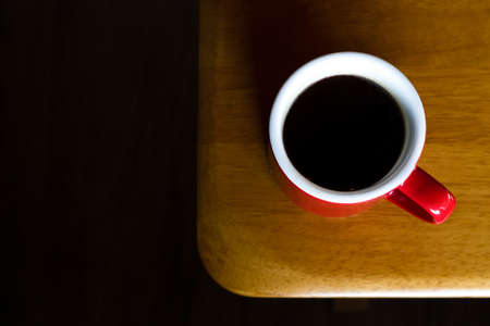 red mug of hot americano black coffee on the top of the wooden table with morning light at the coffee shop. coffee break for refreshing in the working time.の写真素材