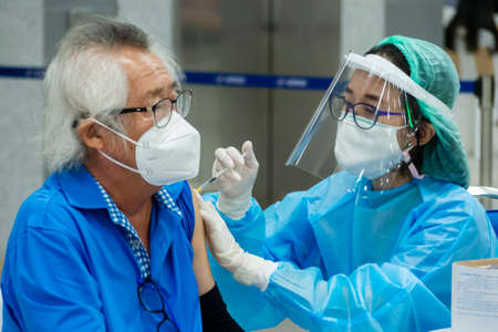 Bangkok, Thailand - September 17, 2021 : asian doctor or nurse giving covid antivirus vaccine shot to senior man patient wearing protective face mask from coronavirus at Bang Sue Grand Station.のeditorial素材