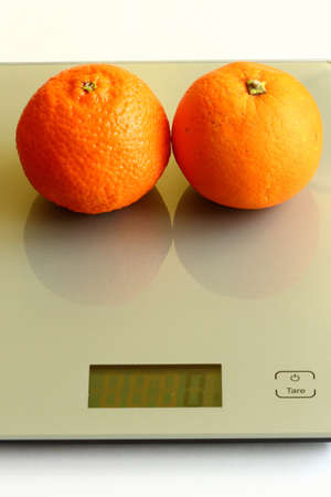 Pair of fresh orange and mandarine on a scaleの写真素材