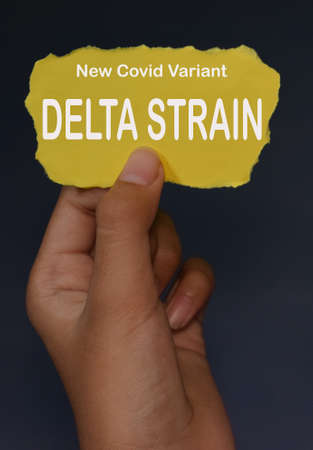 Female left hand is holding yellow paper with text New Covid Variant DELTA  STRAIN. With dark background.の写真素材
