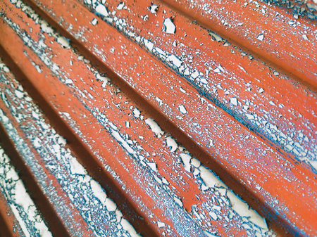 A dynamic diagonal view of a weathered orange corrugated metal surface. The texture features extensive peeling paint revealing light blue layers, rust spots, and sharp ridged patterns for a gritty industrial background.の写真素材