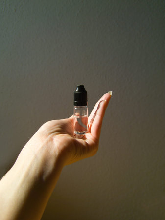 A close-up, minimalist shot of a hand gently cradling a small, transparent bottle with a black...