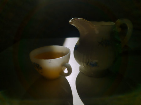 A moody, intimate still life focusing on a vintage porcelain pitcher and a teacup. The soft morning light highlights the textures and evokes a quiet, serene domestic atmosphere for editorial content.の写真素材