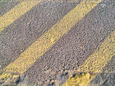 A detailed, high-angle shot of a coarse asphalt road surface featuring distinct, weathered yellow...