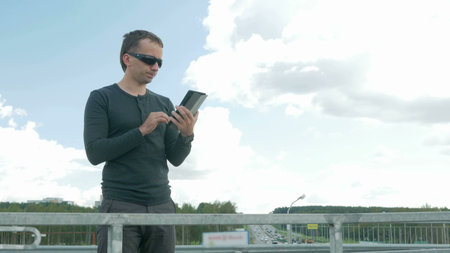 Outdoor portrait of modern young man with digital tablet. A man with glasses on the bridge. Behind...