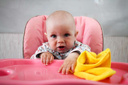 Beautiful baby eats porridge from mom's hand. He is sitting on a pink children's chairの写真素材