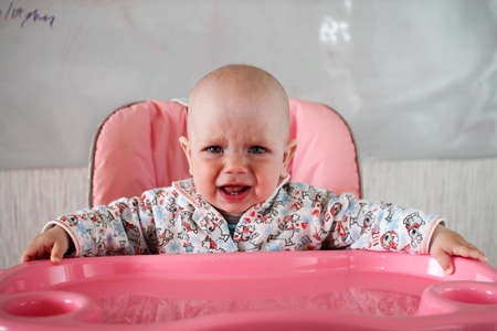 Beautiful baby eats porridge from mom's hand. He is sitting on a pink children's chairの写真素材