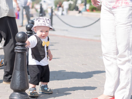 Beautiful toddler walking with his mother on a city holiday. Kid stylishly dressed with a butterfly and a cap.の写真素材