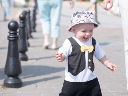 Beautiful toddler walking with his mother on a city holiday. Kid stylishly dressed with a butterfly and a cap.の写真素材