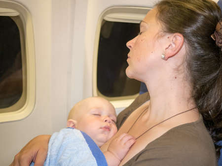 Mother hug and sleep with her newborn baby during flight. Concept photo of air travel with babyの写真素材