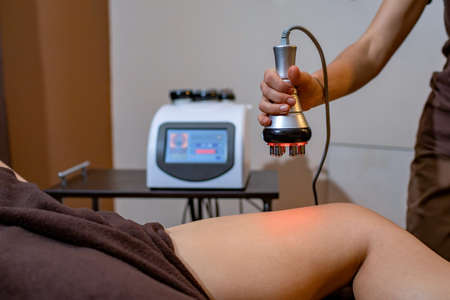 Cosmetology. A young woman with a beautiful body in a spa salon on a massage procedure. Cosmetologist using modern spa treatment machine. Body care and beauty.の写真素材