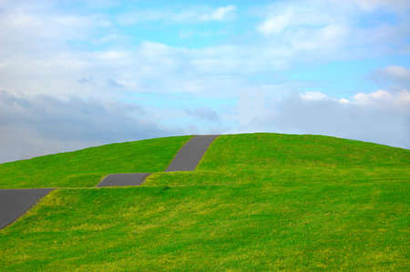 colorful grassland in summer under cloudy sky with path up the hillの写真素材