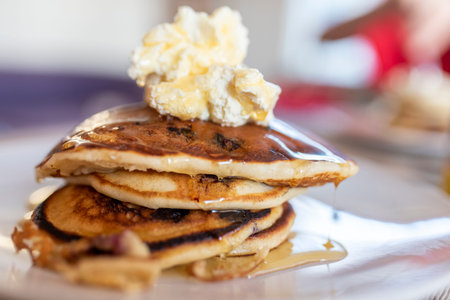 Close-up of American-style blueberry pancakes with cream bacon, and dripping maple syrup.