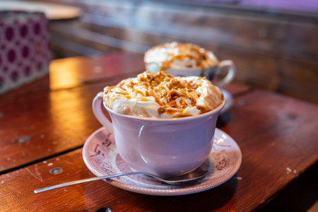 Two cups of fresh hot chocolate topped with whipped cream and salted caramel on a brown wooden...