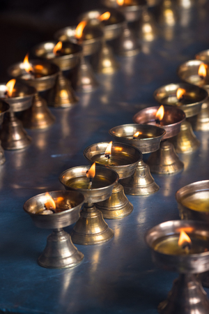 Row of burning candles lighting up at Buddhist temple in Kathmandu, Nepal. Beautiful candle flames lighten up for praying and faith purpose. Select focusの写真素材