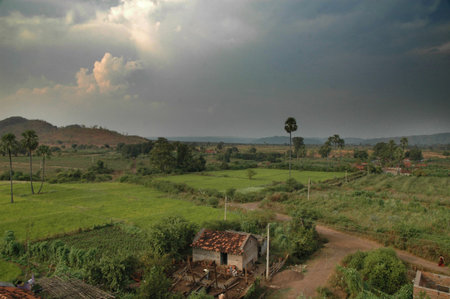 A typical rural landscape full of green fields, rolling hills, mud huts, palm trees, pathways