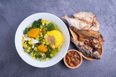 Selective focus of clear spinach soup with corn, sliced ââgarlic, pumpkin in a white bowl, and fried dried fish in Indonesian called sayur bayam bening and ikan asin. Indonesian spの写真素材
