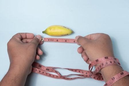 a man's hand is measuring a small banana using a tape measure, small male genitalia size conceptの写真素材