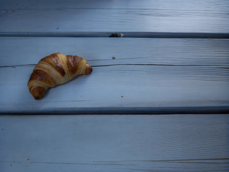 A freshly baked croissant, golden brown and flaky, sits on a rustic wooden surface.の写真素材