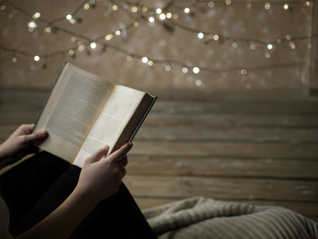 Person relaxing and reading a book at night with fairy lights in the background.の写真素材