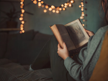 A person relaxes in a comfy chair, reading a book, illuminated by fairy lights.の写真素材