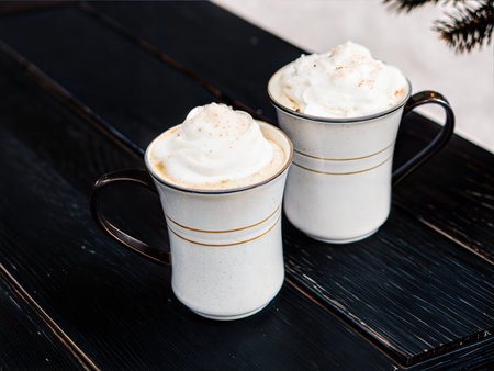 Two mugs of creamy eggnog topped with whipped cream. Cozy winter drink.