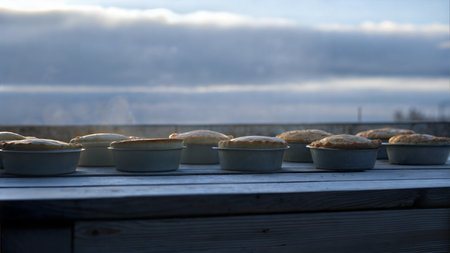 Several freshly baked golden pies sit on a wooden table, with a cloudy sky in the background.の写真素材
