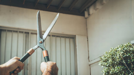 Close-up of hands holding large shears in front of a house and shrubs.