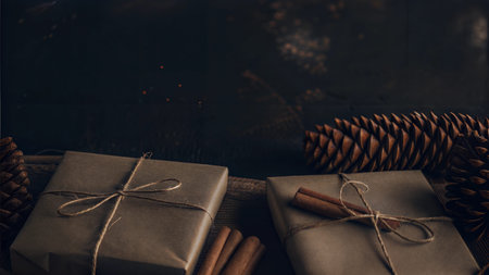 Two gifts wrapped in brown paper tied with twine and cinnamon sticks, surrounded by pine cones.の写真素材