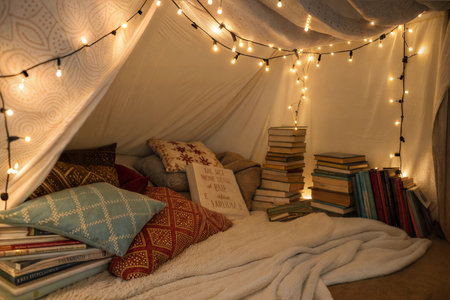 A fort made of blankets, pillows, books, and fairy lights creates a magical reading nook.の写真素材