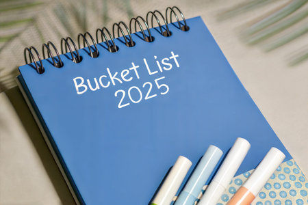 A blue spiral notebook with the words Bucket List 2025 written on it, and colorful markers.