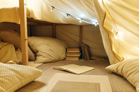 A comfy and well-lit reading space created under a bunk bed, using pillows, blankets, and fairy lights.の写真素材